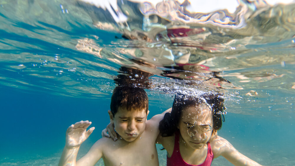 Two kids with closed eyes diving into the sea